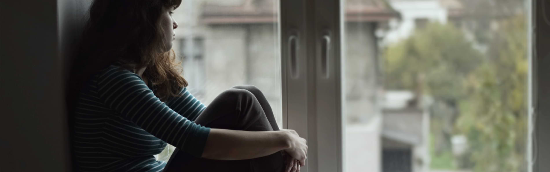 Eine junge Frau sitzt auf einer Fensterbank und schaut aus dem Fenster