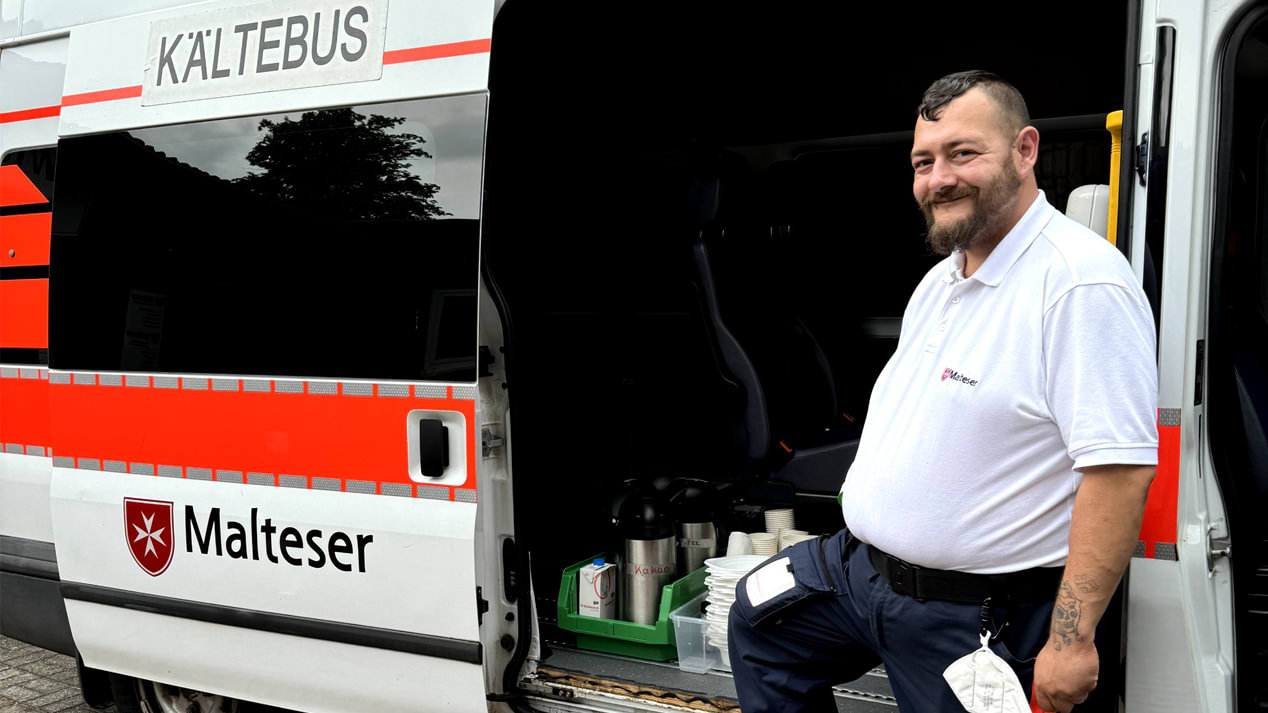 Ein lächelnder Mann vor der offenen Tür eines Rettungswagens mit der Aufschrift „Kältebus“.