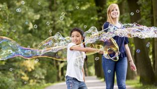 Junge macht große Seifenblasen und wird von Malteser Helferin begleitet.