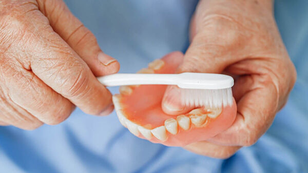Nahaufnahme zweier Hände einer älteren Person, welche ein herausnehmbares Gebiss mittels einer Zahnbürste reinigen.