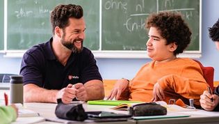 Malteser Schulbegleiter sitzt mit einem Jugendlichen im Rollstuhl im Klassenraum.
