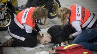 Zwei Schulsanitäter kümmern sich um ein verletztes Mädchen, welche auf dem Boden liegt.