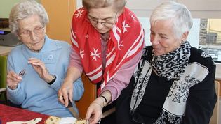 Malteser Helferin gibt zwei älteren Damen ein Stück Kuchen