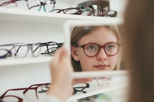 Ein Mädchen mit Brille betrachtet sich in einem Spiegel