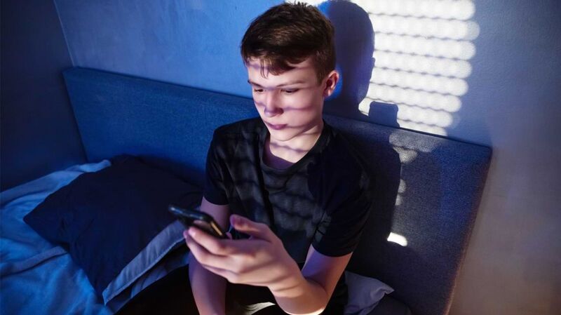 Ein Teenager sitzt in einem Bett und schaut auf ein Smartphone