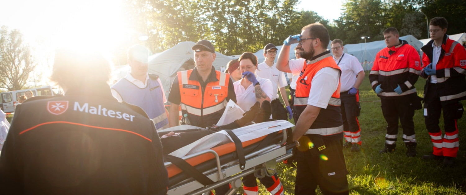 Ehrenamtliche des Malteser Sanitätsdienstes und Katastrophenschutzes tragen eine Person auf einer Rettungstrage.