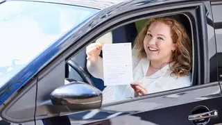 Eine Frau sitzt im Auto und hält den Erste-Hilfe-Nachweis für den Führerschein in den Händen.