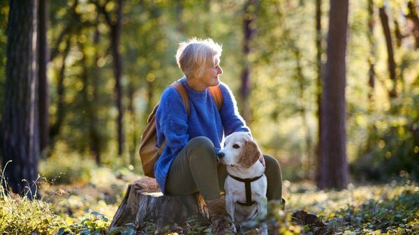 Eine ältere Frau mit Hund in einem Wald.