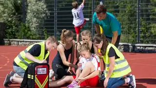 Malteser Schulsanitäter versorgen ein Mädchen, das sich beim Sport verletzt hat.