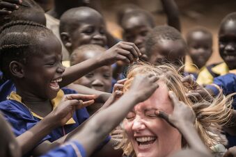 Junge Frau wird von Kindern im Sudan umringt, die ihre Haare berühren möchten