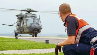 Malteser Helfer hockt auf dem Boden und schaut auf einen landenden Hubschrauber.