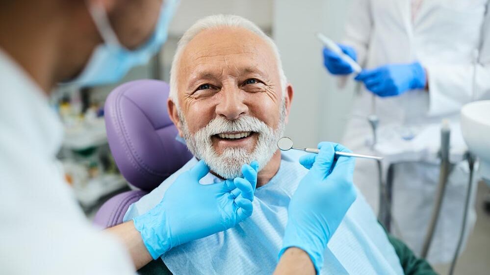 Ein älterer Mann wird von einem Zahnarzt untersucht und lächelt dabei.
