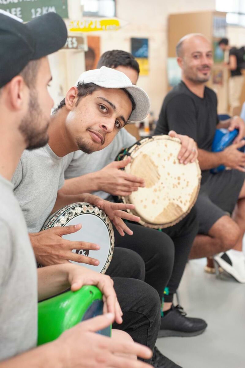 Junge Männer spielen auf Stühlen sitzend auf Trommeln.