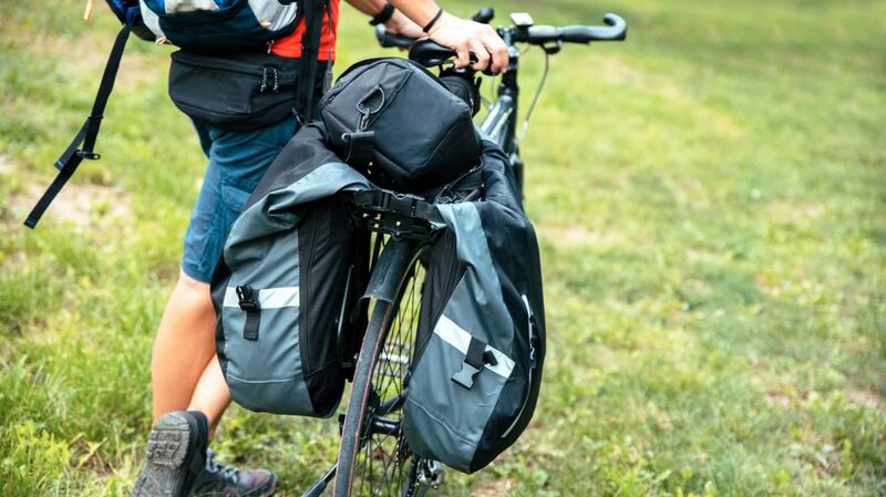 Ein Mann schiebt ein Fahrrad mit Satteltaschen über eine Wiese